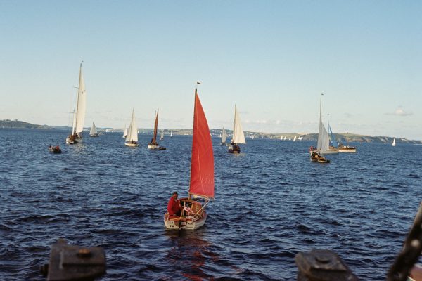 A red boat (Tinkerbelle) surrounded by six other craft on the sea