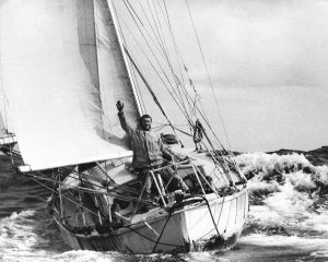 A black and white image of Sir Robin Knox-Johnson aboard his yacht 'Suhaili' in the sea, returning to Falmouth